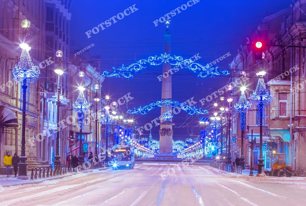На фотографии изображён Невский проспект, украшенный яркой новогодней иллюминацией. На переднем плане выделяется праздничный обелиск «Городу-герою Ленинграду», подчёркивающий историческую значимость места. Улицы покрыты свежим снегом, а свет гирлянд создаёт атмосферу зимнего торжества. Этот пейзаж символизирует праздничный дух Санкт-Петербурга в период Рождества и Нового года.